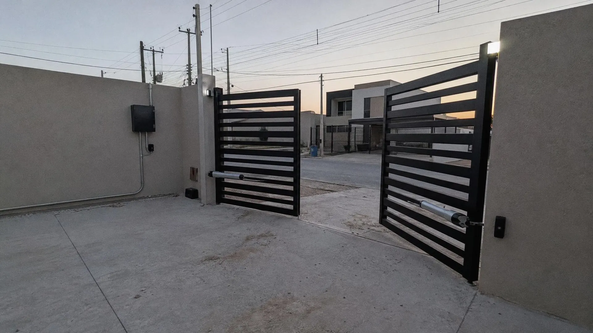 Portón de herrería de dos hojas con pistones automáticos, abriéndose al atardecer